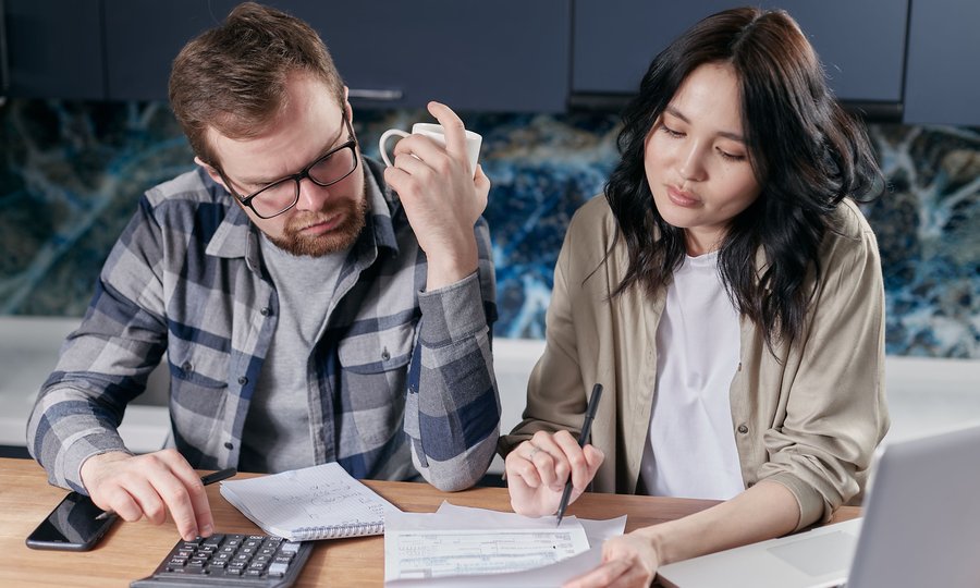 Finanças do casal: casal organizando o orçamento da casa com calculadora e laptop