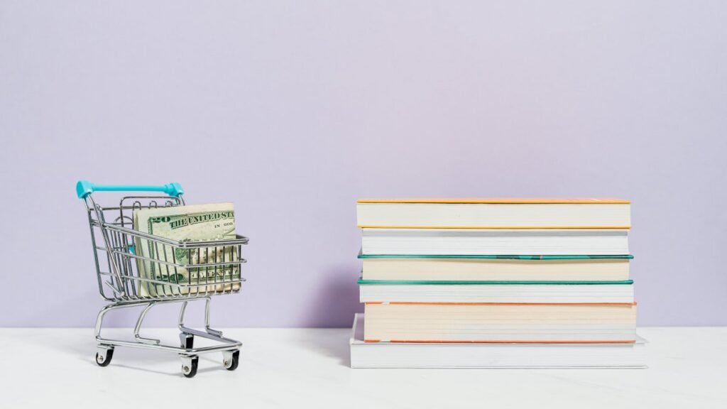 Pilha de livros para sair das dívidas ao lado de carrinho com dinheiro
