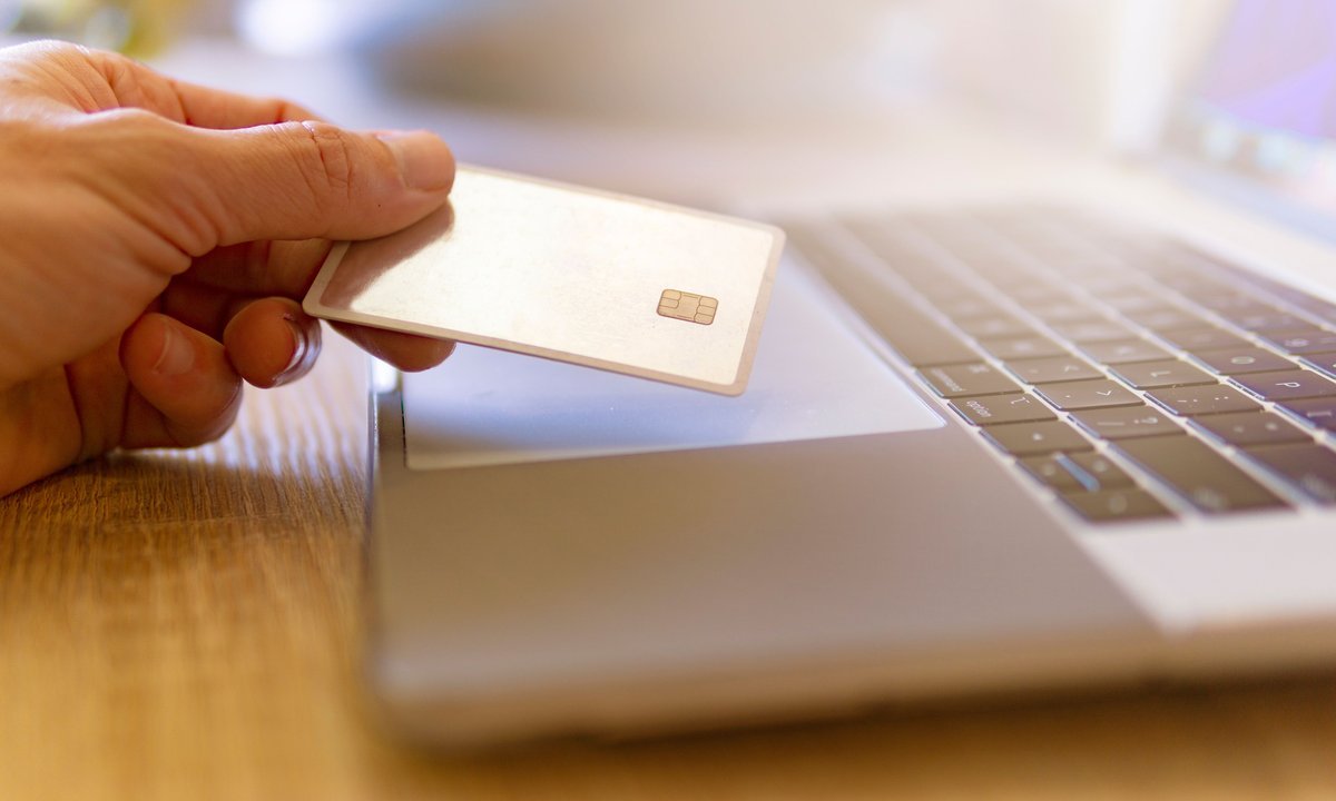 Pessoa com cartão de crédito na mão diante do notebook escolhendo o melhor dia para comprar no cartão