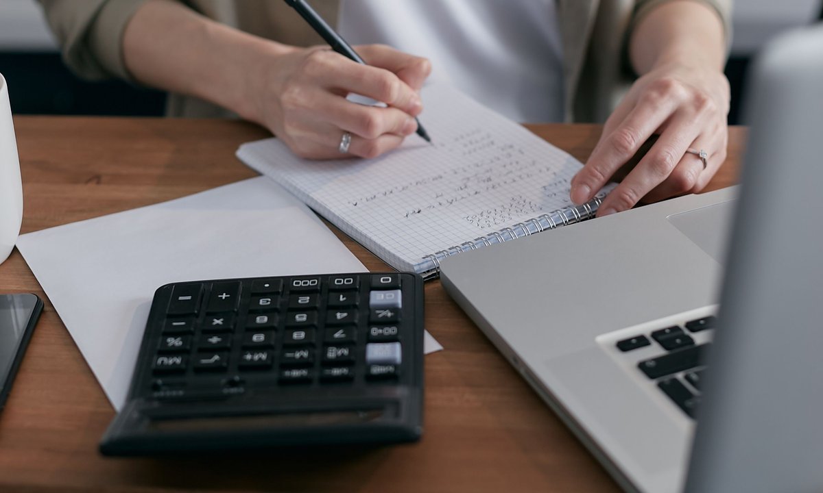 Pessoa anotando valores com calculadora e notebook para comparar CLT ou PJ