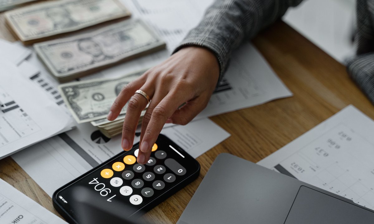 Mão digitando numa calculadora sobre contas e papéis, cálculo da dívida para o Desenrola 3.0