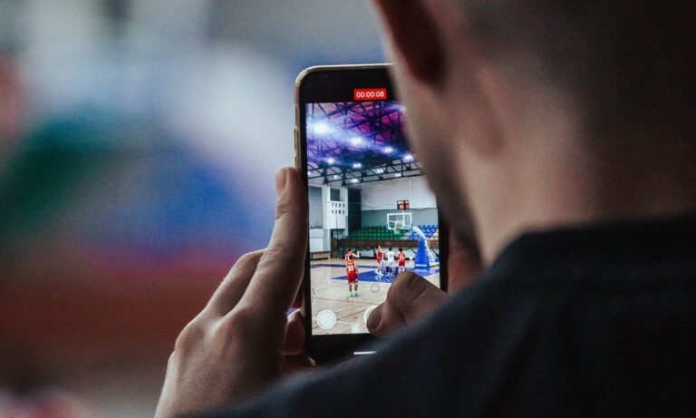 Homem segura celular com partida esportiva na tela, tema do saldo das bets