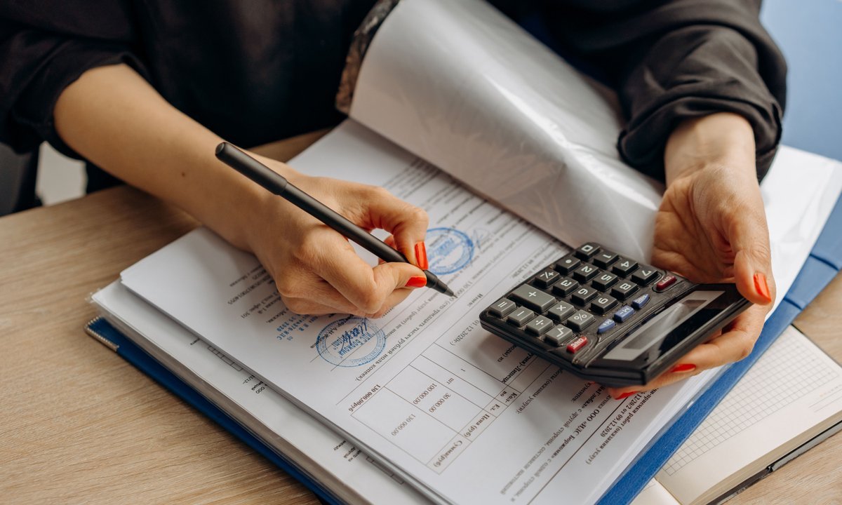 Pessoa calculando o come-cotas de novembro com papéis e calculadora
